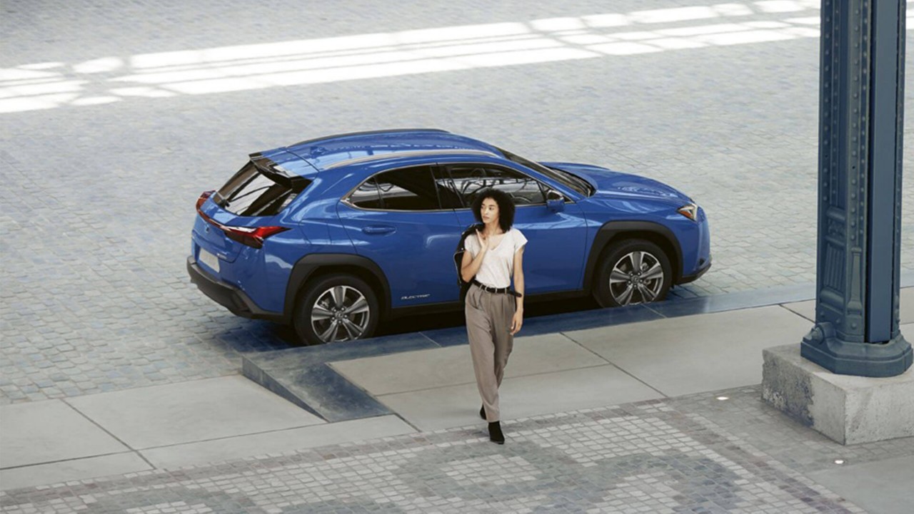 A woman walking away from a parked Lexus UX 300e